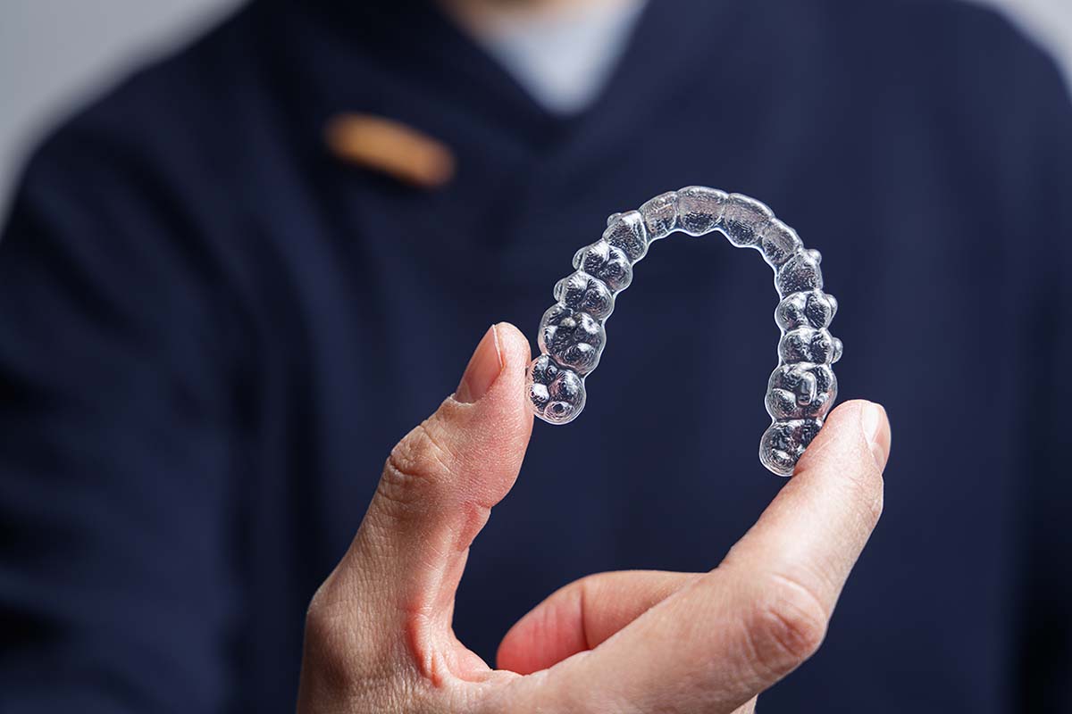 Kelleher Orthodontics specialist holds an Invisalign Teen clear aligner, demonstrating the transparent treatment option.