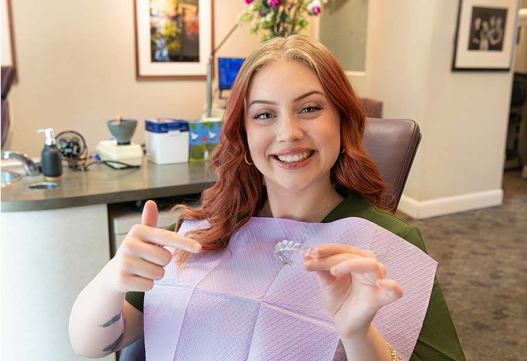Patient smiling while holding Invisalign clear aligners from Kelleher Orthodontics for a confident, straighter smile.