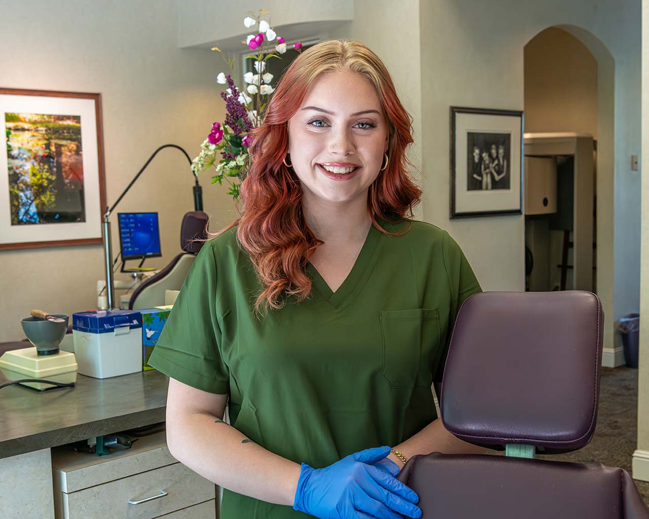 A friendly Kelleher Orthodontics team member smiles next to a patient chair, welcoming new patients.